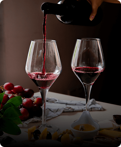 red wine being poured into glasses beside grapes and cheese