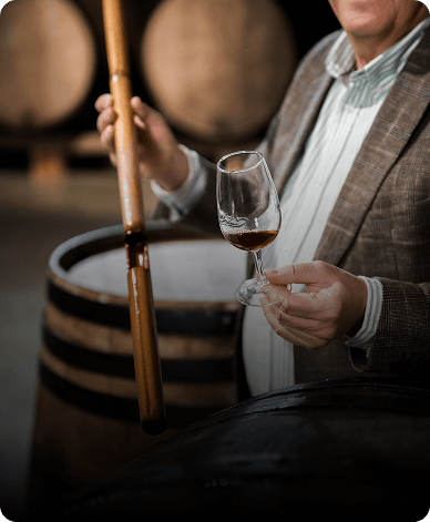 person drawing wine from an oak barrel into a tasting glass