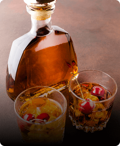 decanter of amber spirits beside two cocktails with citrus garnishes